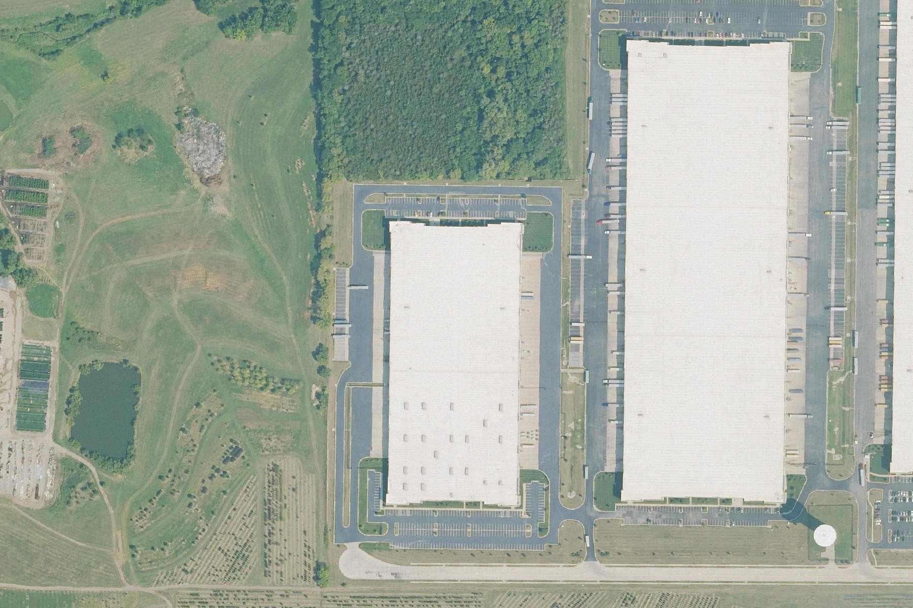 Overhead view of a very large rectangular distribution warehouse with truck courts and trailer bays on two sides, set in a logistics park beside rail infrastructure.
