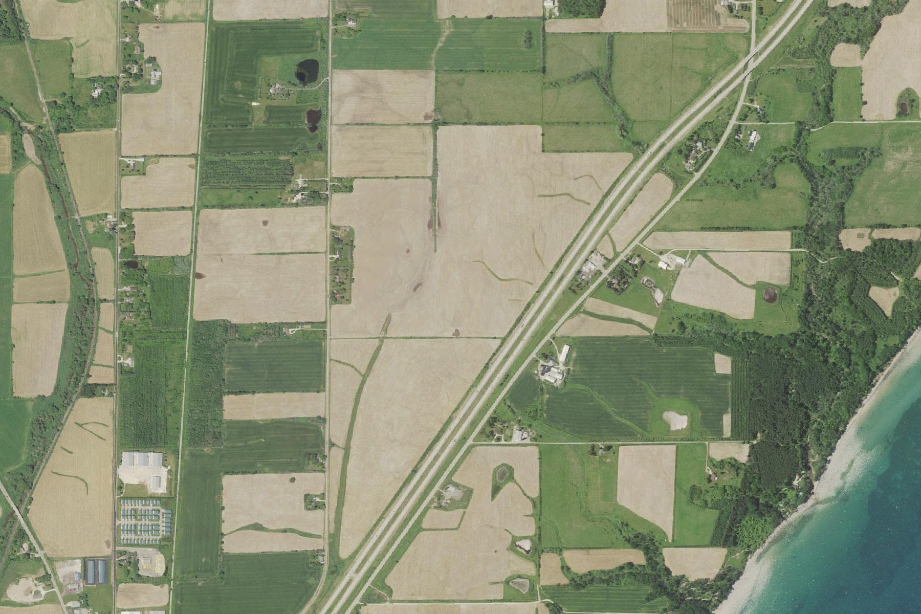Overhead view of a wide block of open farm fields on a section-road grid roughly a mile inland from a large lake, crossed by an interstate highway.