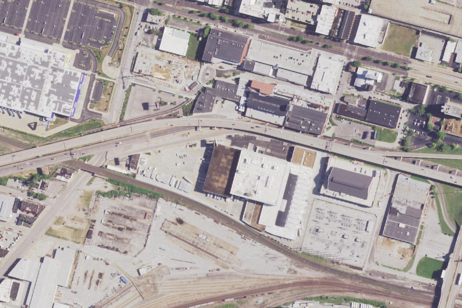 Overhead view of dense urban blocks along a highway, with warehouses, an elevated interstate, and a wide fan of railway tracks running through the lower half of the frame.