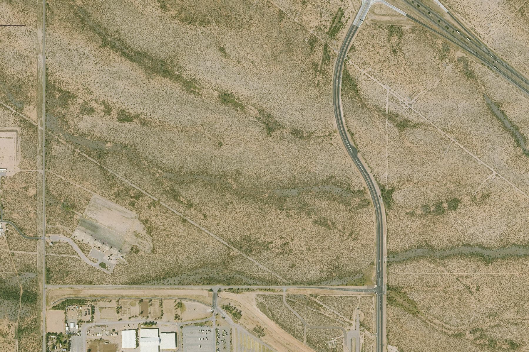 Overhead view of flat undeveloped Sonoran desert scrub crossed by straight section roads, with a fairground complex and scattered industrial buildings nearby.